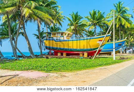 The large painted fishing boats are drying at the road in shade of palms Peraliya Sri Lanka.