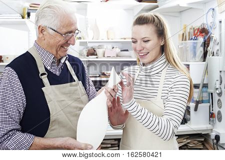 Senior Man With Teacher Looking At Vase In Pottery Class