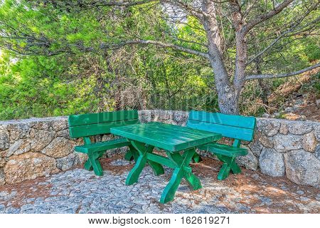 The resting place with a green wooden benches and table in Tucepi old village in the slope of a mountain Biokovo, Croatia.