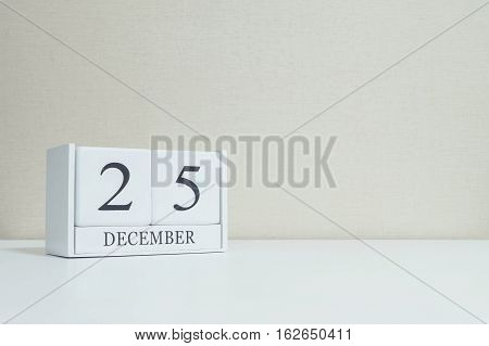 Closeup white wooden calendar with black 25 december word on blurred white wood desk and cream color wallpaper in room textured background with copy space selective focus at the calendar