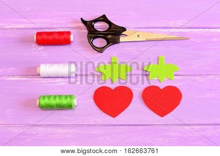 How to hand sew a children toy strawberry. Step. Tutorial. Parts cut from red and green felt in the shape of strawberries and leaves. Scissors, thread on a wooden table. Fun sewing lesson. Top view