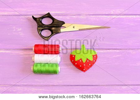 How to hand sew a children toy strawberry. Step. Tutorial. Children soft toy strawberry stitched from felt and embellished with beads. Scissors, thread on a wooden table. Kids sewing lesson. Top view