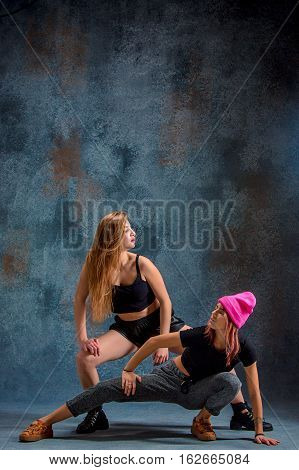 The two attractive girls dancing twerk iat the blue studio background