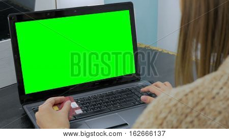 Young woman buying goods from the internet and entering number security code from credit card on laptop with green screen. Online, technology and internet concept.