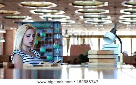 Schoolgirl or student reads aloud the book sitting at a table in the library