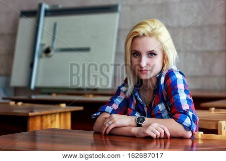 The obedient disciple sits at a table in the classroom. Seen against the background of the Board for drawing