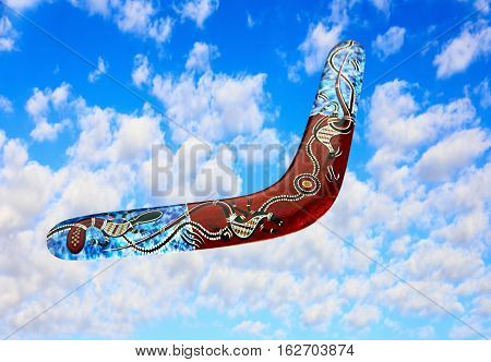 Multicolored australian boomerang flies in sky against of pure white clouds.