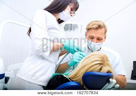 Dentist man with assistant treats teeth patient in hospital office