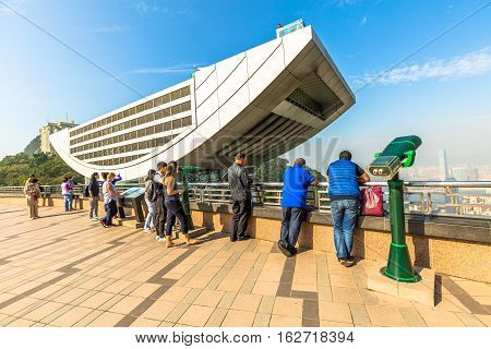 Hong Kong, China - December 7, 2016: Tourists observe the Hong Kong skyline from the free viewing terrace of Peak Galleria, a gigantic shopping center in front of the Peak Tower.
