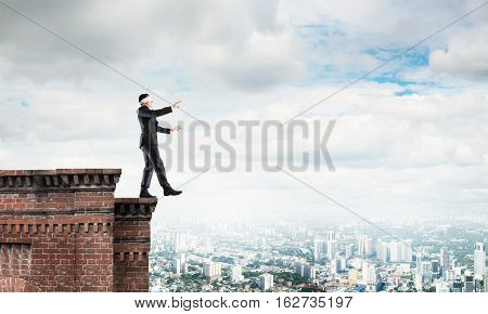 Businessman with blindfolder on eyes walking on building top