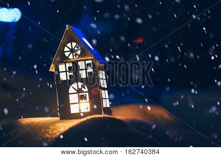 Lantern house with burning candle on snow in the evening.
