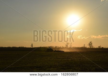 Tractor At Sunset Plow Plow A Field. Tilling The Soil In The Fall After Harvest. The End Of The Seas