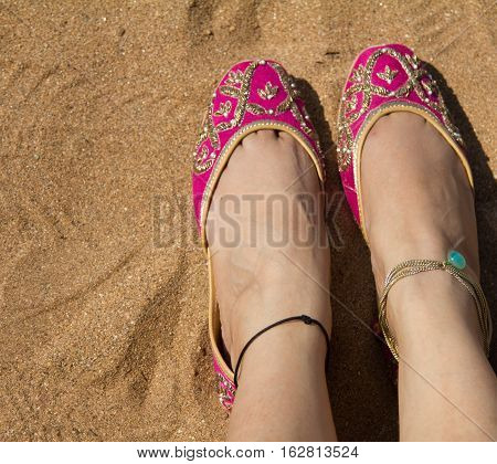 A lady wearing a pair of pink traditional Indian women's shoes (jutis) at the Anjuna beach in north Goa, India