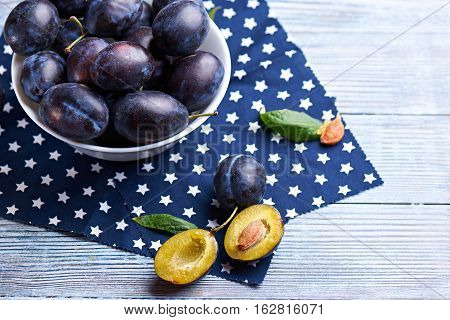 Fresh organic plums in ceramic bowl on rustic wooden table at dark napkin with stars.