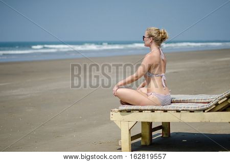 blonde girl in a bikini sitting on a sun lounger on the ocean