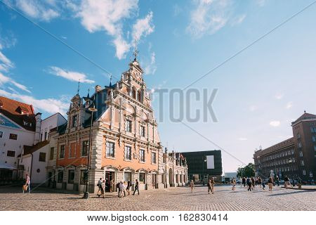 Riga, Latvia. Side View Of The Schwabe House At Town Hall Square, Ancient Historical Landmark And Popular Touristic Showplace With Walking People In Summer Sunny Day Under Blue Sky
