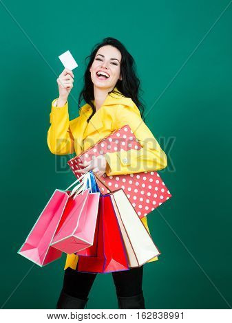 Happy pretty girl or beautiful woman young sexy cute fashion model with brunette hair with shopping bags shows blank credit or discount card on blue wall