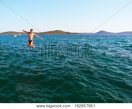 Beach activities. Boy jumping into the sea.