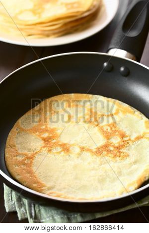 Freshly made crepe in frying pan with a stack of crepes in the back photographed with natural light (Selective Focus Focus in the middle of the crepe in the pan)