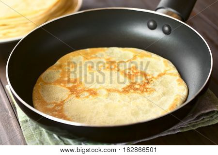 Freshly made crepe in frying pan with a stack of crepes in the back photographed with natural light (Selective Focus Focus in the middle of the crepe in the pan)
