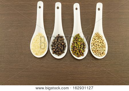 Green bean white sesame black and white pepper in white ceramic spoon on black wooden background