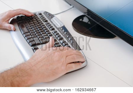 Hands on keyboard with monitor at side