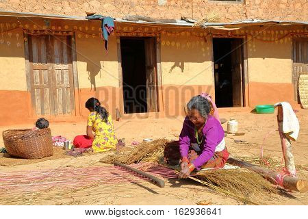 DHULIKHEL, NEPAL - DECEMBER 25, 2014: Nepalese old woman making traditional woven bed (using straw) in the countryside near Dhulikhel