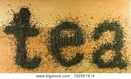 The word tea is laid out on a light-brown wooden Board small leaf black tea. Board is the background for the word tea.
