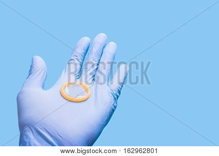 Hand in glove holding a condom. Doctor and contraceptives. Blue background