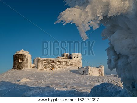 Frosted old Polish observatory on Pop Ivan Mount (Ukraine) against blue sky background. Little man form shows lardge building size.