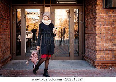 Young Female Student In Warm Autumn Clothes Coming Out Of The House With A Backpack With Books And A