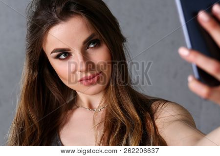 Beautiful European Woman Portrait. Worth A Gray Background Uses A Smartphone Makes Selfie And Reads 