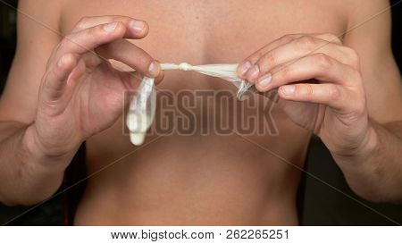 Close-up. Men's Hands Hold The Used Tied Condom. The Concept Of Safe Sex And Contraception.