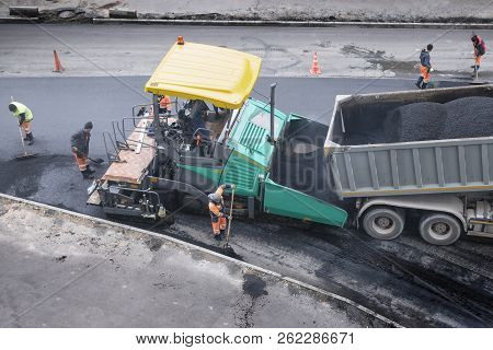 Asphalt Paver Machine Places A Layer Of New Asphalt. Dumper Unloads Asphalt. A Cold Autumn Day. Road