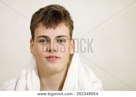Handsome smiling boy teenager in a towel on shoulders poses in white studio