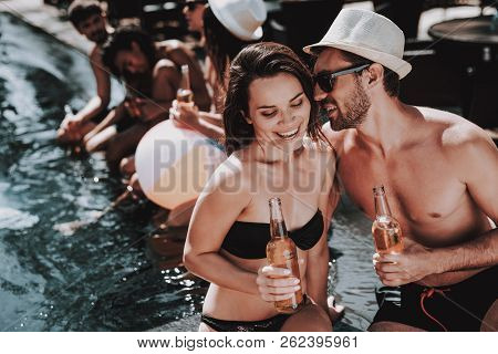 Smiling Couple With Alcoholic Drinks At Poolside. Beautiful Young Couple Holding Bottles Of Beer And