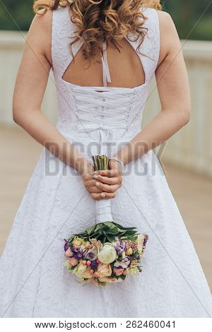 The Bride Is Holding Her Bouquet On The Background Of A Wedding Dress