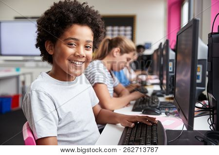 Portrait Of Smiling Male Pupil Sitting In Line Of High School Students Working at Screens In Computer Class