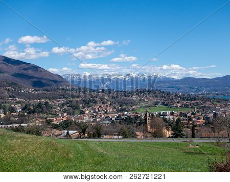 Panoramic View Of The Lake, Mountains With Snow And A Small Town. Alpine Valley, Erba, Como, Lombard