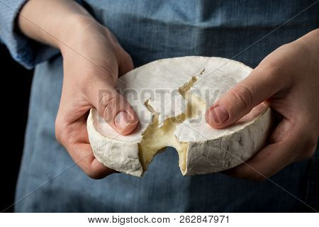 Woman In Blue Apron Holding Soft French Camembert Cheese On Dark Background