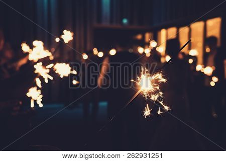 Close Up Of A Bengal Light At The Blurred Background Of People Standing With Burning Sparklers In Se