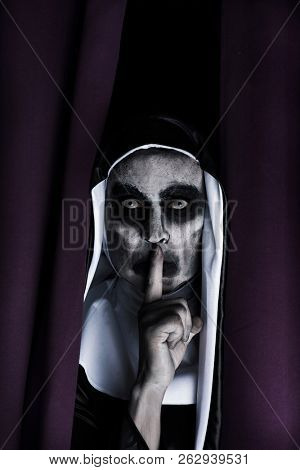 closeup of a frightening evil nun, wearing a typical black and white habit, peeping out from a purple curtain, asking for silence