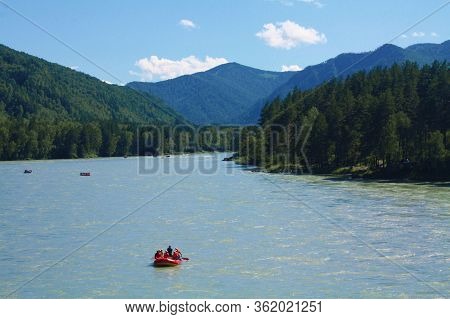 Rafting On The Katun River. A Red Boat With People Rafting Along A Wide And Raging River. Entertainm