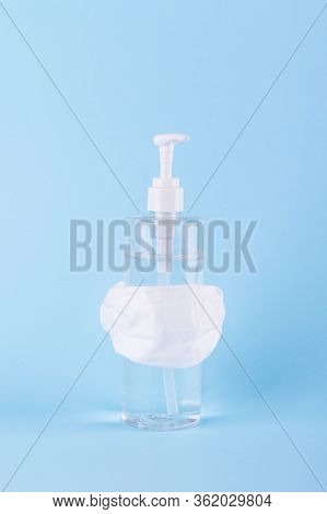 Gel Hand Sanitizer Is Wearing A White Surgical Mask On A Blue Pastel Background. Antiseptic Antibact