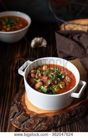 Bean Soup With Meat And Vegetables Served On A Rustic Board And Wooden Table With Bread And Garlic. 