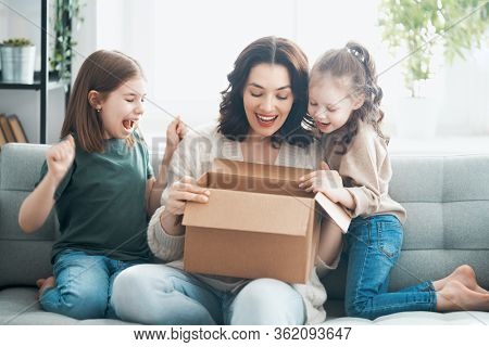 Mother and daughters are unpacking cardboard box at home.