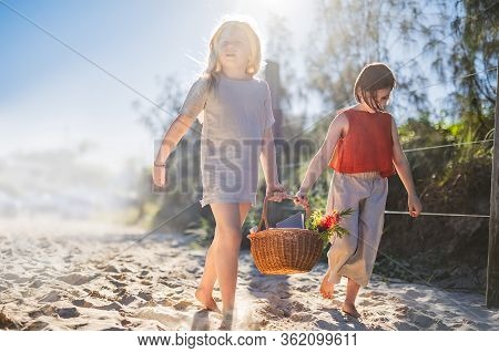 Little Girls Walking Barefoot On The Sand And Caring A Picnic Basket Together. Summer Leisure, Love 