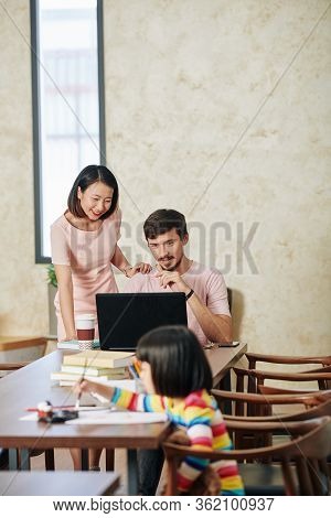 Little Girl Painting When Her Parents Looking At Laptop Screen When Shopping Online
