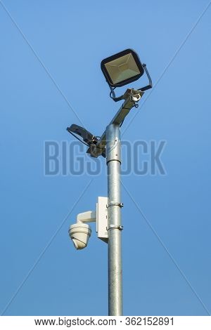 Security Camera And Floodlights Mounted On Mast Against A Blue Sky