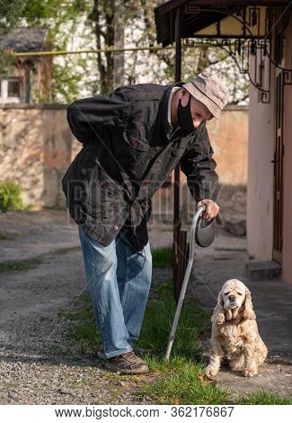 Senior Man In Protective Mask With A Cane Walking With A Dog In Sunny Day